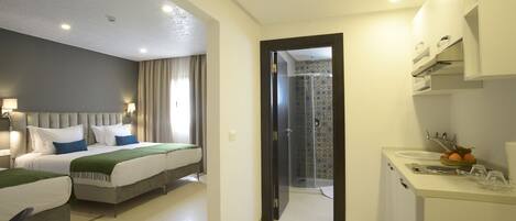 A hotel room with two beds, a bathroom with a shower, and a kitchenette.