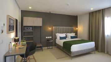 A modern hotel room with a bed, desk, chair, and a small kitchenette.