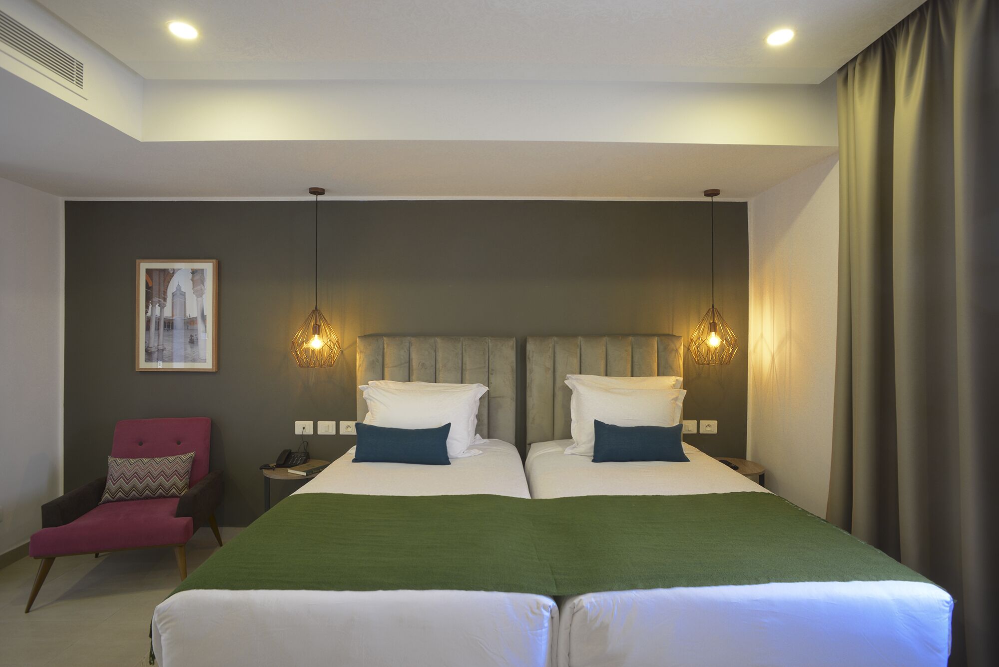 Un letto matrimoniale con una coperta verde, due comodini con lampade, una sedia e un quadro incorniciato appeso al muro.