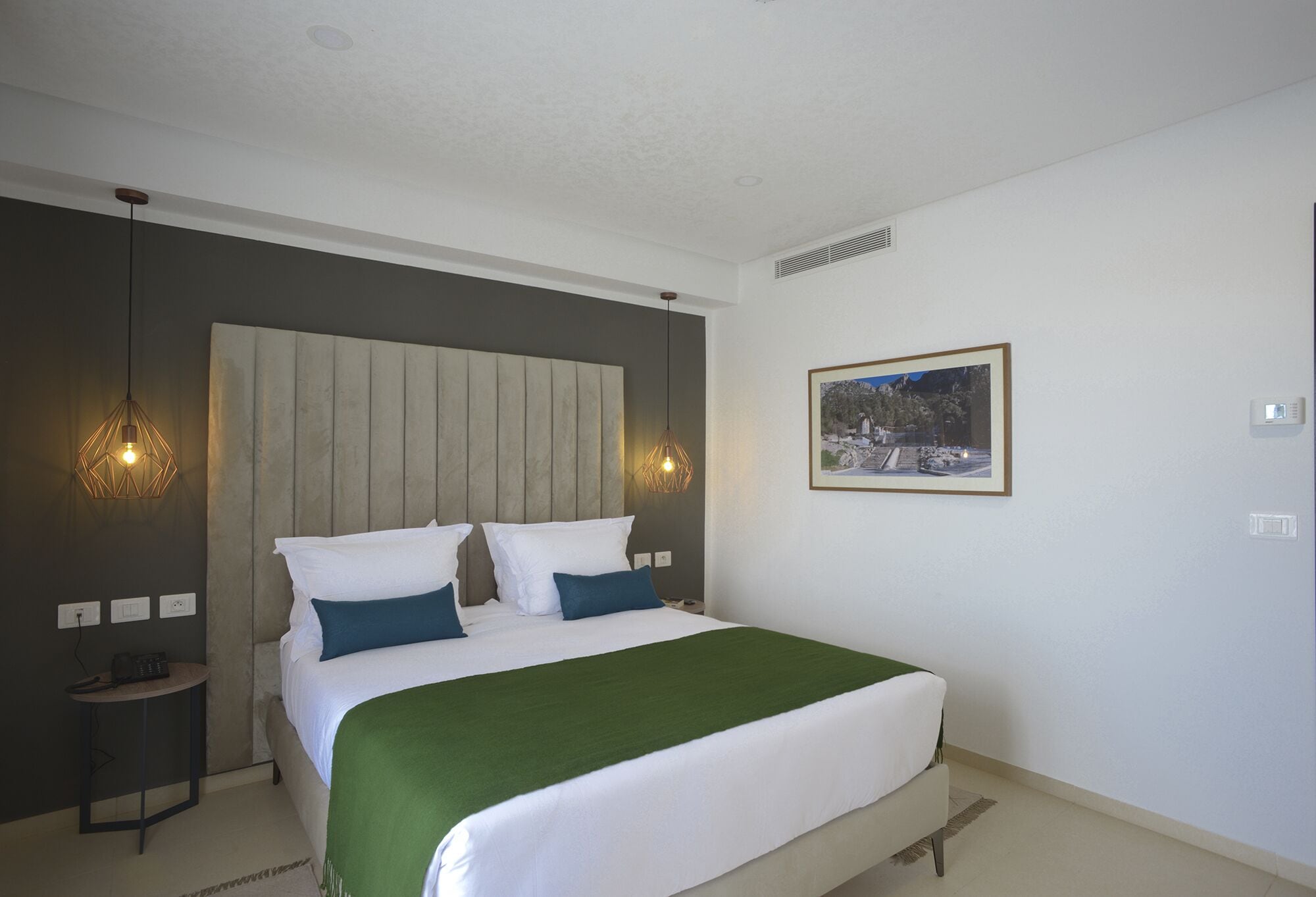 A bedroom with a bed, a nightstand, a wall-mounted picture, and a pendant light.