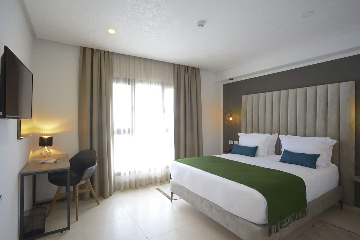 Une chambre d’hôtel avec un lit, un bureau, une chaise, une télévision et une fenêtre avec des rideaux.