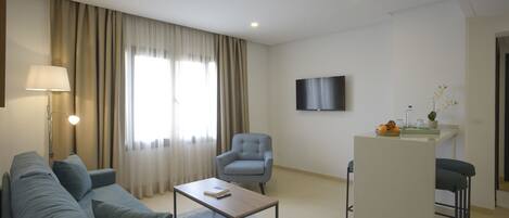 A modern living room with a sofa, armchair, coffee table, and a small kitchen area with a bar stool.