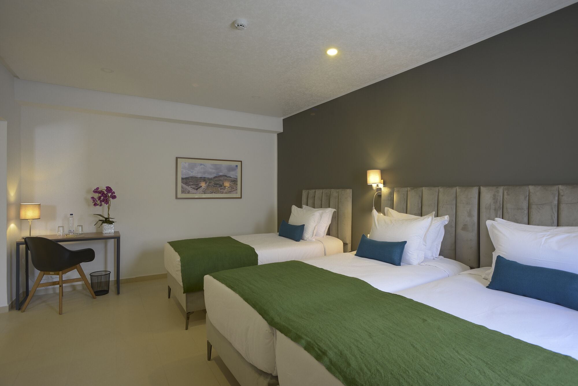 Een hotelkamer met twee bedden, een bureau, een stoel, een lamp en een lijstje aan de muur.