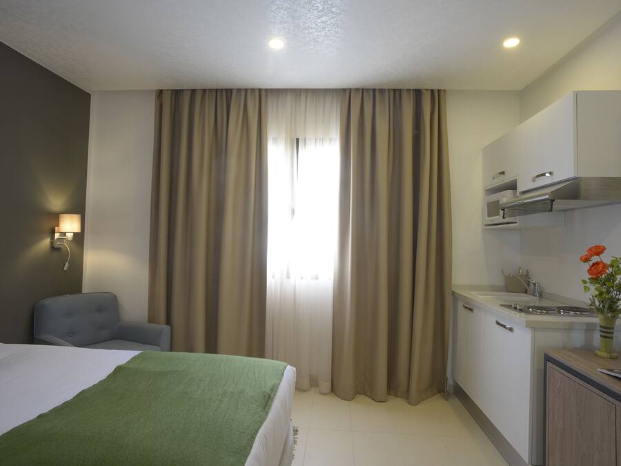 Habitación de hotel con cama, una silla, kitchenette y ventana con cortinas.