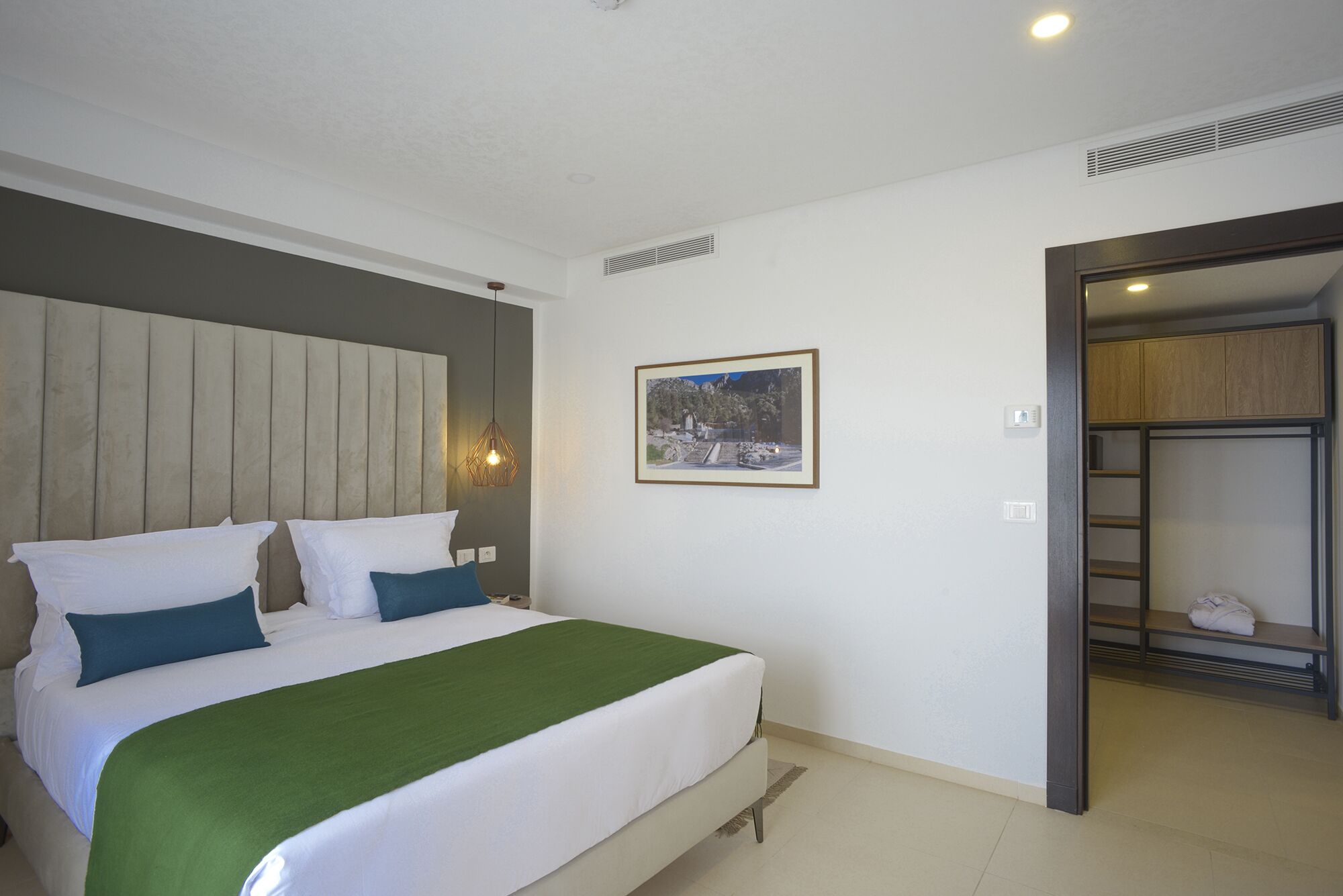 A bedroom with a bed, a green throw blanket, and a framed picture on the wall.