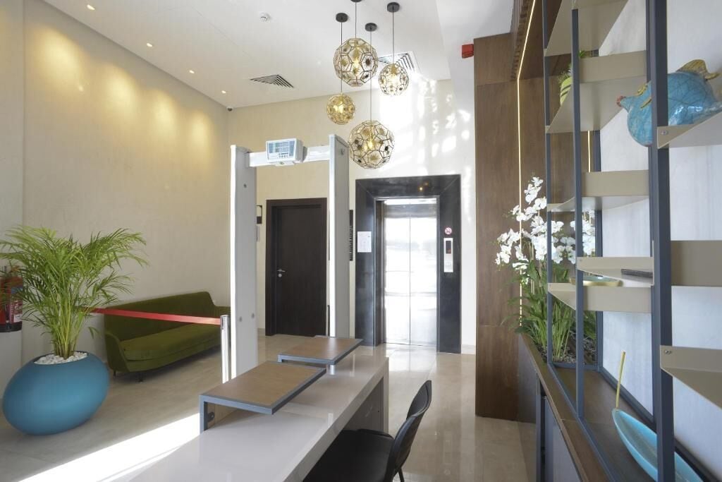 A modern reception area with a reception desk, a green sofa, potted plants, and a staircase with decorative items.