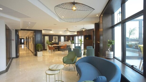 A modern hotel lobby with a curved blue sofa, round tables, and a large ceiling fan. - Maia Hotel Suites (Tunis)
