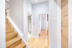 Un pasillo con piso de madera, paredes blancas y una escalera de madera.