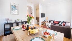 Een moderne woonkamer met een houten ontbijttafel, een bank en een televisie op de achtergrond.
