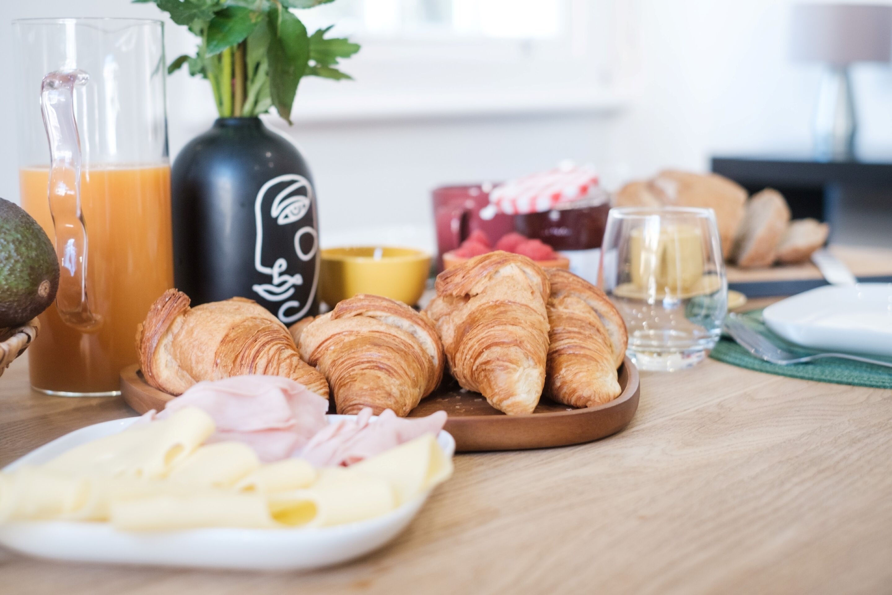 Ein Frühstückstisch mit Croissants, Käse, Schinken und Saft.