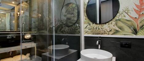 A modern bathroom with a glass-enclosed shower, a round mirror, and a large sink.
