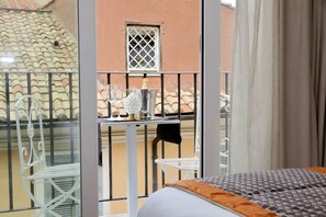 A balcony with a metal table, a chair, and a bed with an orange pillow. - HELMIRAGE PIAZZA DI SPAGNA SUITE (Rome)
