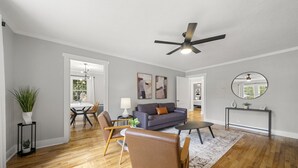 Una sala de estar amplia con piso de madera, ventilador de techo, un sofá, una mesa de centro y una zona de comedor con sillas y una mesa.