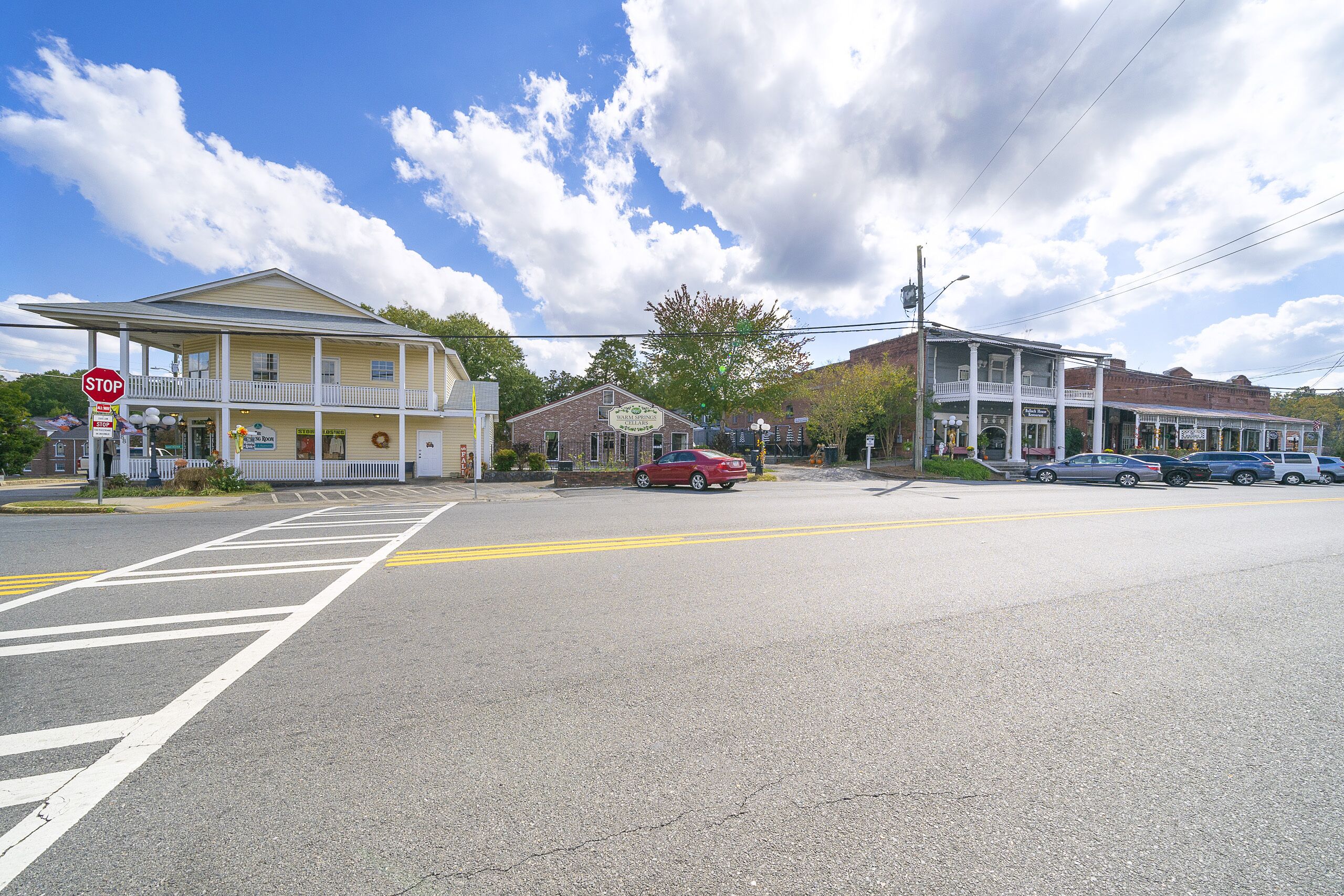 A street intersection with a two-story building featuring a porch and a sign for 'Warm Springs Cellars'.