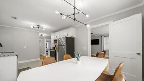 Una cocina moderna con armarios blancos, un refrigerador de acero inoxidable y un comedor con una mesa blanca y sillas marrones.