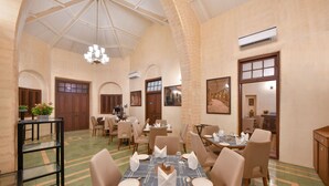 A spacious dining area with multiple tables and chairs, a chandelier, and an arched ceiling. - Arova Woods Zinc Journey by The Fern (Mawal)