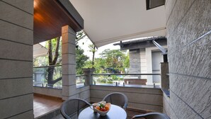 A balcony with a table and chairs, a bowl of fruit, and a view of the outdoors. - Arova Woods Zinc Journey by The Fern (Mawal)