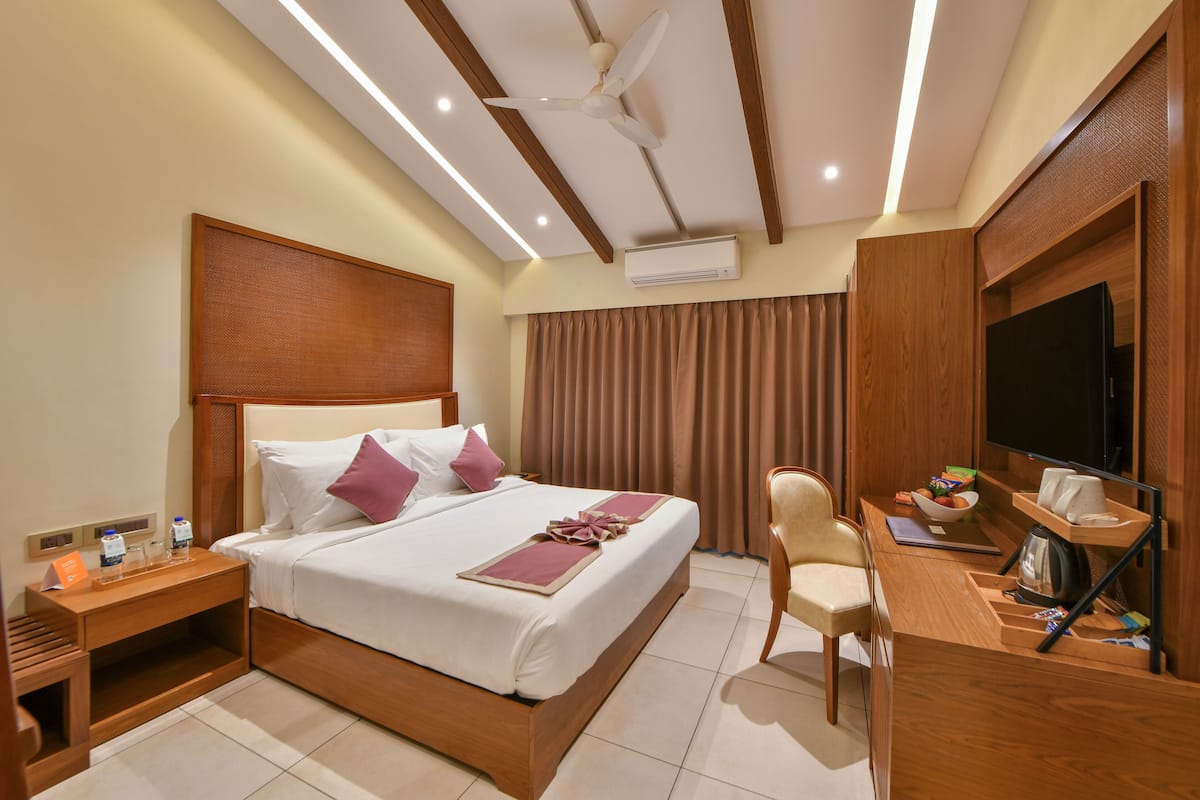 A hotel room with a bed, a desk with a chair, a television, and an air conditioning unit.
