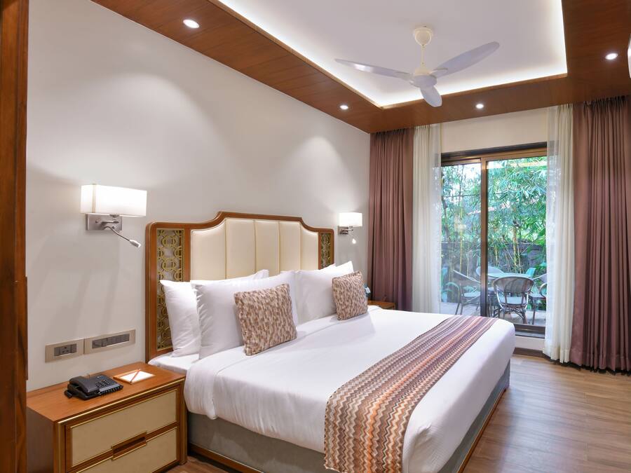 Amplia habitación de hotel con una cama grande, un ventilador de techo y vistas al exterior a través de una puerta corrediza de vidrio.