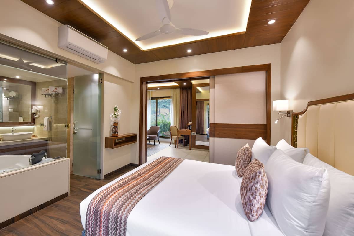 A hotel room with a large bed, a bedside table, a mirror, a ceiling fan, and a view of the outdoors.
