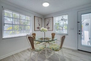 A dining area with a glass table surrounded by wicker chairs, framed artwork on the walls, and a door with a window view.