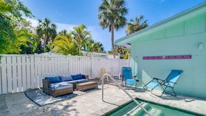 A backyard with a swimming pool, a white fence, a blue lounge chair, and a wicker sofa with blue cushions. - Private Pool - Anna Maria Hideaway by SeaBreeze Vacation (Holmes Beach)