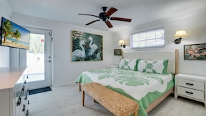 A bedroom with a bed, a ceiling fan, a bench, a nightstand, a lamp, a painting, and a door with a view of the beach. - Private Pool - Anna Maria Hideaway by SeaBreeze Vacation (Holmes Beach)