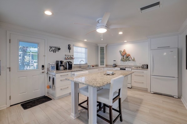 A modern kitchen with white cabinetry, a granite countertop island, and a ceiling fan.