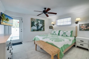 A bedroom with a bed, a ceiling fan, a window with blinds, a bedside lamp, and a door with a view of the outside.