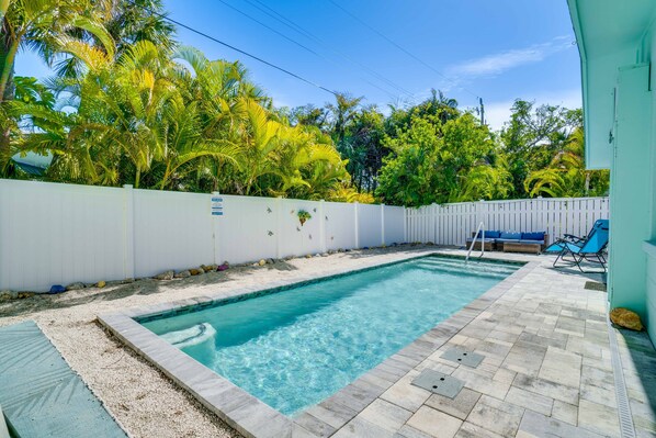 Une piscine entourée d’une clôture blanche, bordée d’une végétation luxuriante et dotée d’une terrasse carrelée.