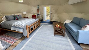 A tented accommodation room with a bed, a sofa, a coffee table, and a view of the outdoors. - Seasonal, Cozy Geo-Dome with Heat/AC on Private Hiking paradise in Gunks. (Wallkill)