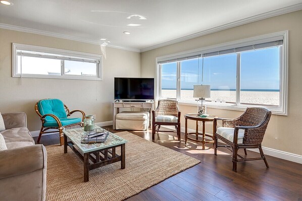 A living room with a TV, wicker chairs, a coffee table, and a view of the beach.