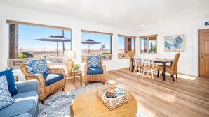 A spacious living room with wicker furniture, a wooden coffee table, and large windows offering a beach view.