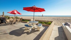 Un patio con mobiliario exterior, una parrilla y sombrillas rojas con vista a una playa.