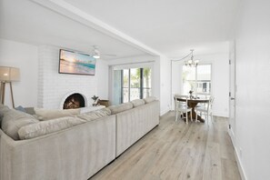 A spacious living area with a fireplace, a large window, and a dining area with a chandelier.