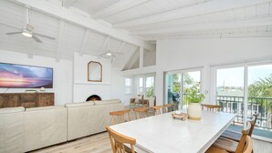 Een ruime woonkamer met een witte bank, een eettafel met houten stoelen, een open haard en een grote televisie.