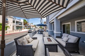 Un patio exterior con mobiliario de mimbre, una chimenea y sombrillas a rayas.