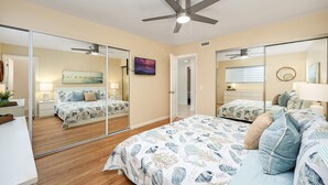 Un dormitorio con una cama grande, ventilador de techo, televisión y espejo.