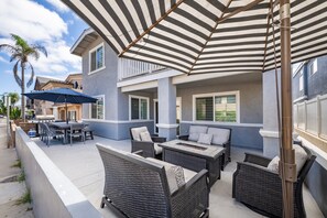 Un patio al aire libre con mobiliario de mimbre, una parrilla y toldos a rayas.