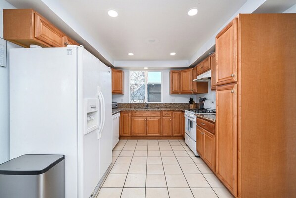A modern kitchen with wooden cabinets, a white refrigerator, a stove, and a dishwasher. - 6 Bedroom home located 2 houses in from the Beach (Newport Beach)