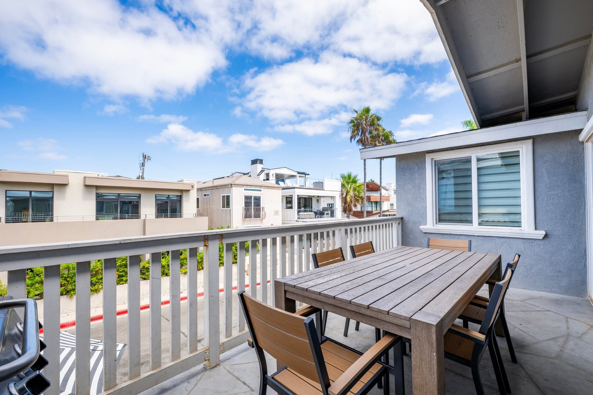 A balcony with a wooden table and chairs, a white railing, and a view of neighboring buildings.