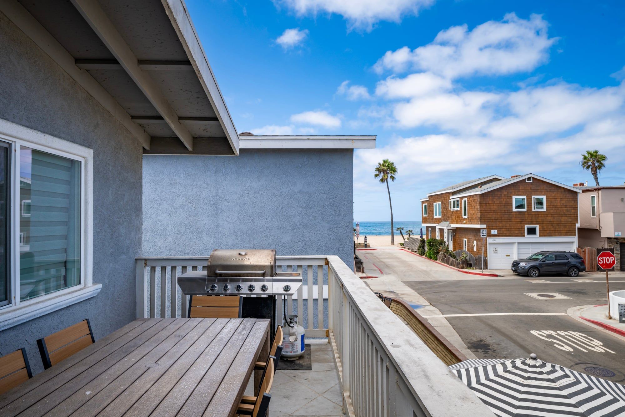 A balcony with a grill, a table, and a view of the beach and ocean.