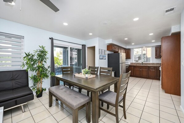 A modern kitchen with wooden cabinets, a black refrigerator, and a dining area with a table and chairs. - Giant Home Sleep 20, Perfect for Multi Family Vacation steps from the Sand (Newport Beach)
