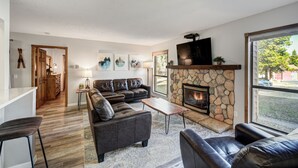 A modern living room with a stone fireplace, leather sofas, and a large window offering a view of the outdoors.