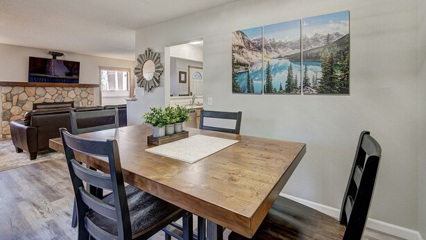 A dining area with a wooden table, chairs, and a stone fireplace. There is a painting of a mountain landscape on the wall.