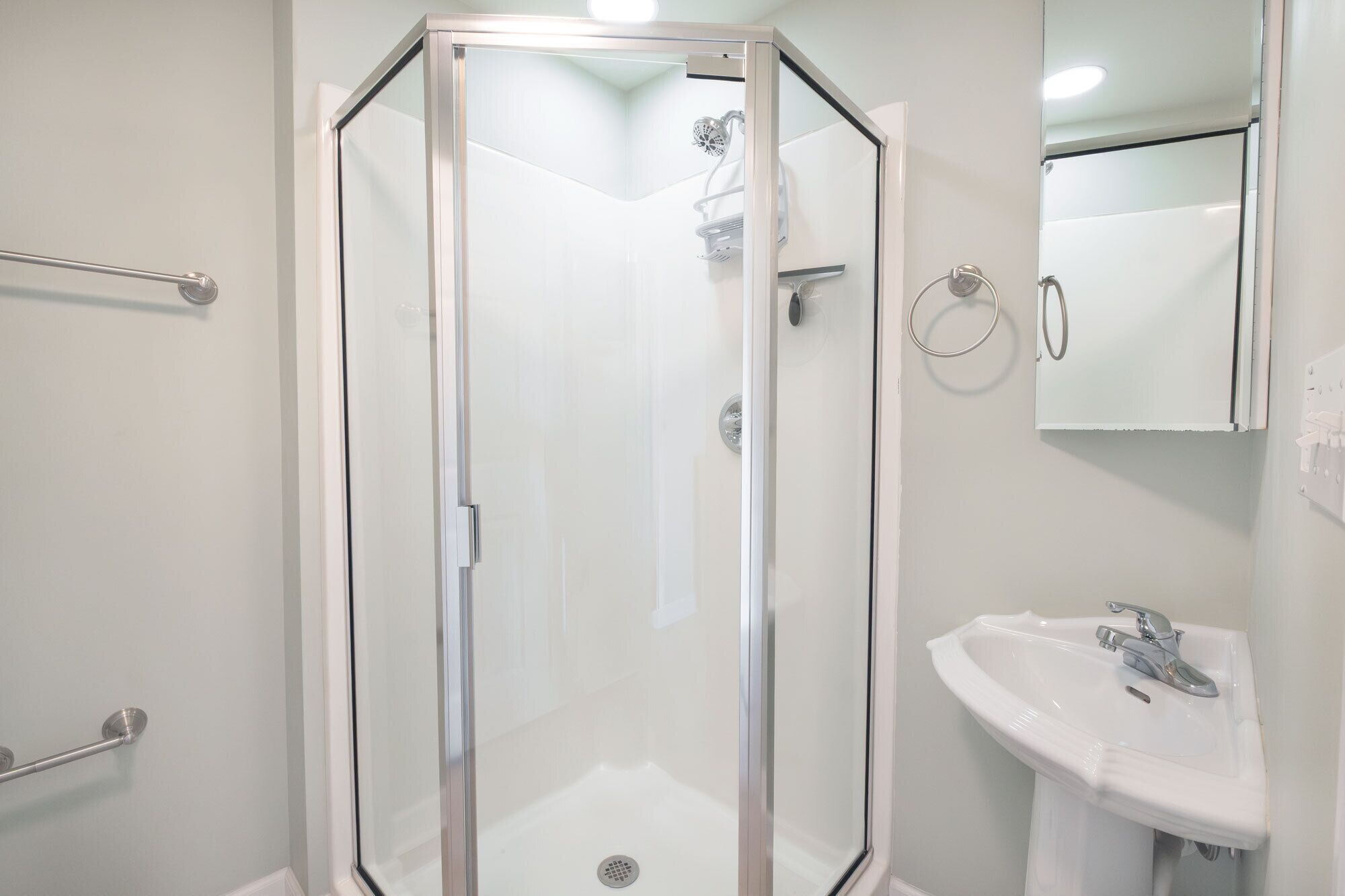 Un baño moderno con ducha de vidrio, lavamanos blanco y un espejo.