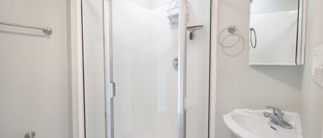 Un baño moderno con ducha de vidrio, lavamanos blanco y un espejo.