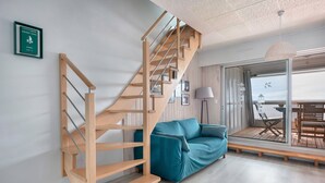 Een moderne woonkamer met een houten trap, een blauwgroene bank en uitzicht op de omgeving door een glazen deur.