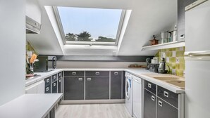 Een moderne keuken met een dakraam, grijze kastjes, een wasmachine en een koffieapparaat.