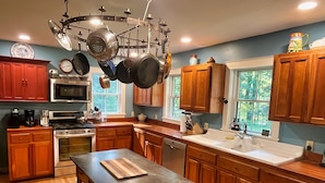 A kitchen with wooden cabinets, a stove, an oven, a microwave, a sink, and a hanging pot rack. - Edgewood, Beautiful custom built 5 bdrm home w/ fire pit, game room, scenic pond (Milford)